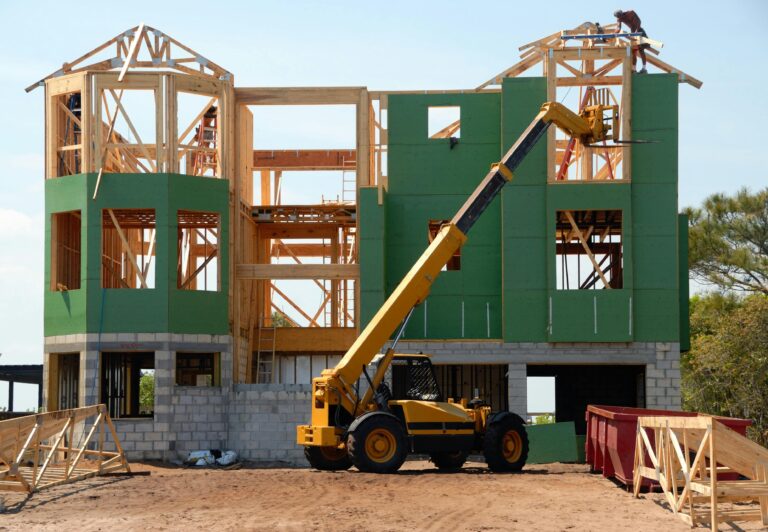 A multi-story wooden house under construction using a crane on a sunny day.